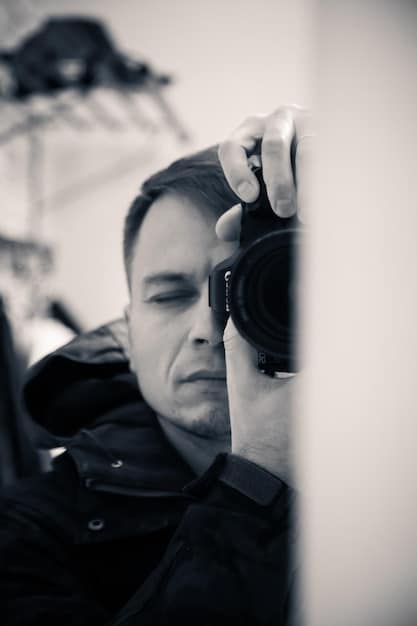 A close-up shot of a cinematographer adjusting the lens of a camera on set. The background is blurred, but the focus is on the intricate mechanics of the camera and the cinematographer's focused gaze.