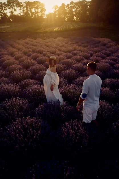 A sun-drenched field of lavender in full bloom, with a young couple standing hand-in-hand in the distance. The focus is on the vibrant colors and the soft, diffused light that bathes the scene.