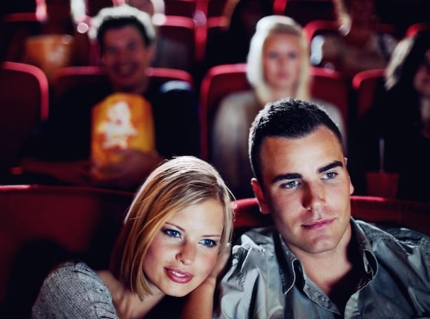 A split-screen image. One side shows a family in a crowded movie theater watching a superhero film. The other side shows the same family comfortably watching a superhero show on a streaming service at home. The contrast highlights the changing viewing habits and preferences.