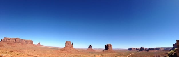 A panoramic view of Monument Valley, Utah, with iconic sandstone buttes rising from the desert floor. The image should capture the grandeur and timelessness of the Western landscape.