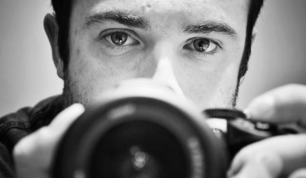 A close-up shot of the director looking through the camera lens, with a determined and focused expression. Capture the intensity and passion they bring to their craft.