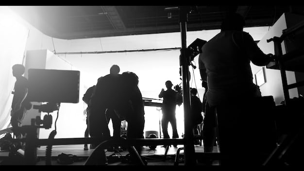 A film crew working on a movie set, with cameras, lights, and various equipment visible. The atmosphere appears tense and focused, with people communicating in hushed tones.