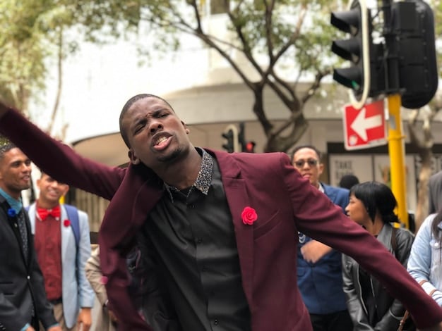 Candid photo of Kanye West addressing a crowd at a 2020 campaign rally. He's wearing a casual outfit, and the crowd behind him is a mix of supporters and onlookers.