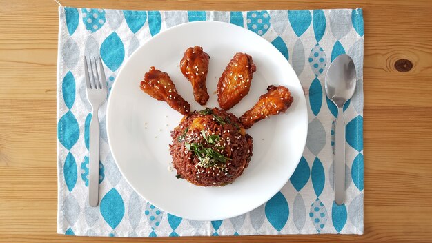 A plate of Korean fried chicken pieces, some plain and some coated in a red, slightly glossy sauce. The chicken is garnished with sesame seeds and displayed on a modern white plate.